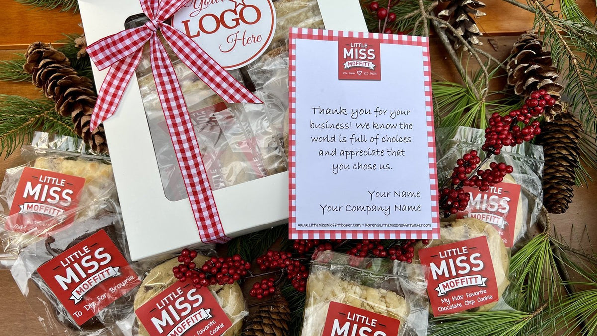 White gift box of individually wrapped Little Miss Moffitt cookies and bars tied with red gingham ribbon, with a thank-you note card and pine branches