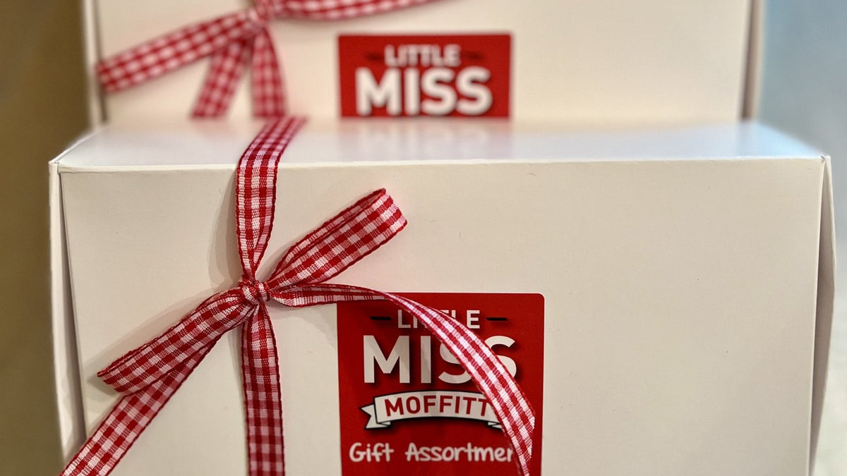 White gift boxes tied with red gingham ribbon and red Little Miss Moffitt Gift Assortment labels, lined up in a row