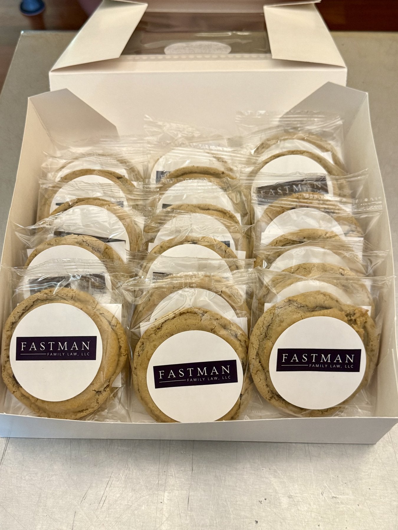 Open gift box of individually wrapped cookies, each one carrying a custom round label with a company logo